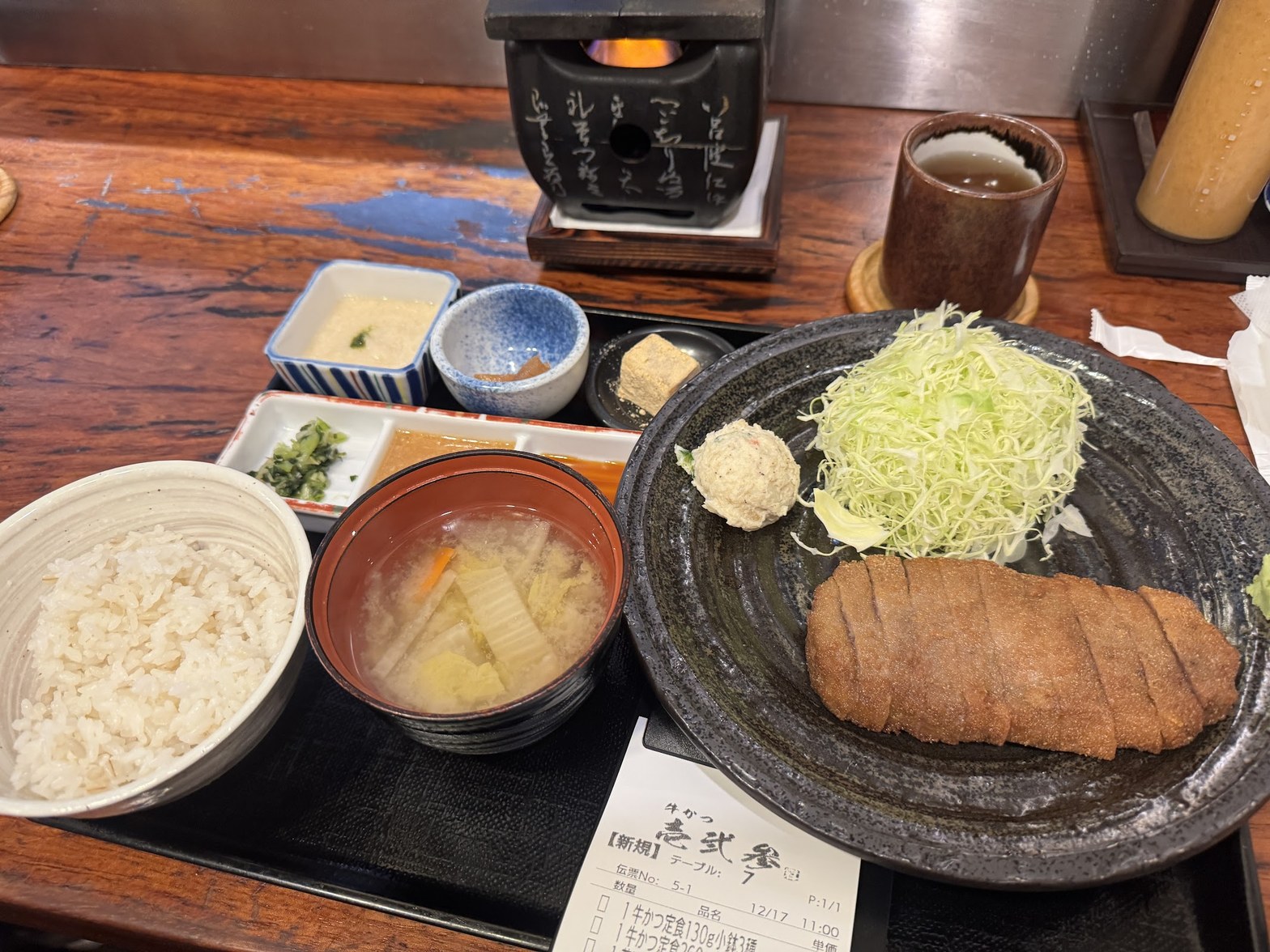 石焼きプレートの炎と牛かつ定食一式、手前に伝票「牛かつ壱弐参」が見える