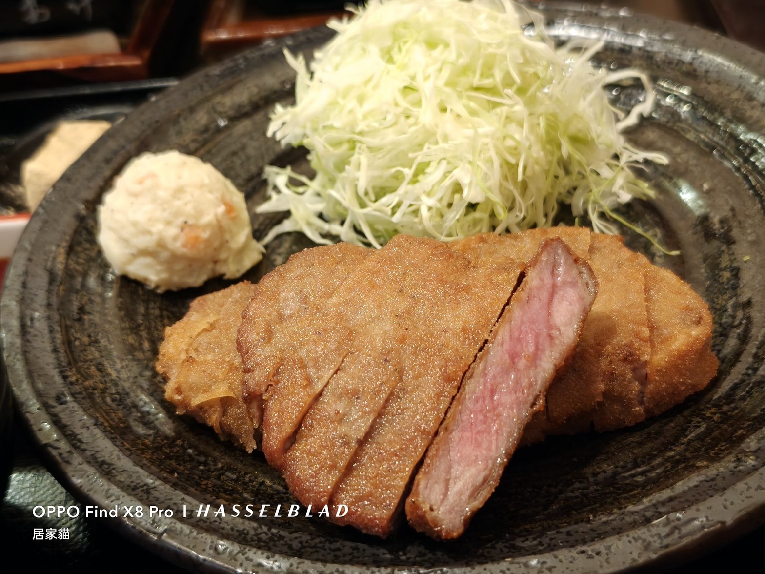 黒い石皿に盛られた牛かつの断面——薄い衣の下にロゼ色の肉が見え、千切りキャベツとポテトサラダが添えられている
