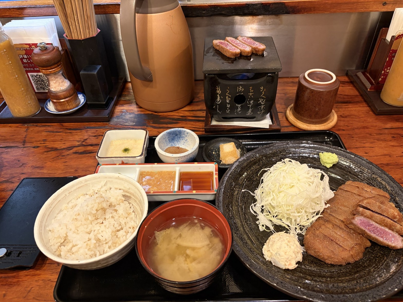 カウンター席の上に置かれた石焼きプレートにロゼ色の牛かつ切れが3枚乗り、麦飯・味噌汁・小鉢が手前に並ぶ